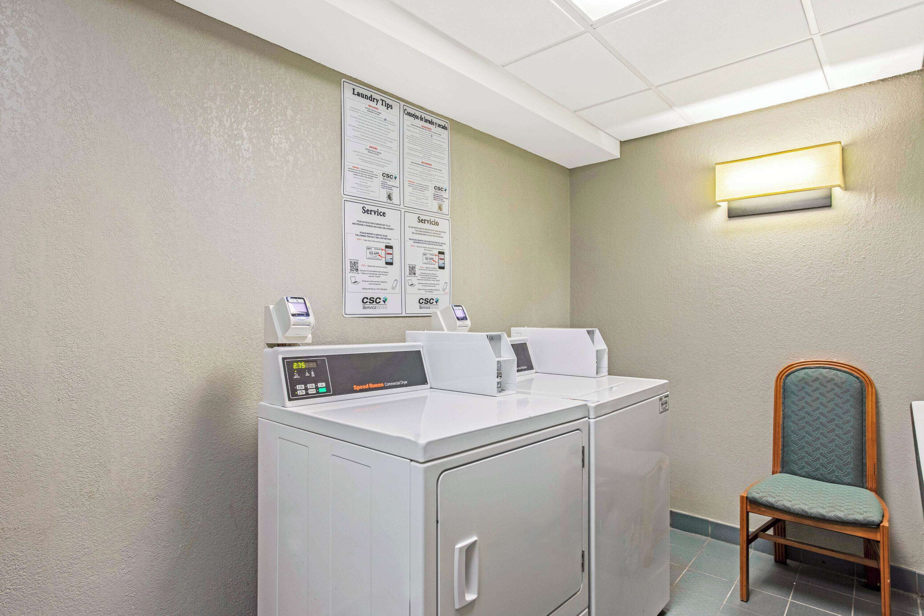 A laundry area with two washing machines, a chair, and a wall-mounted light fixture.