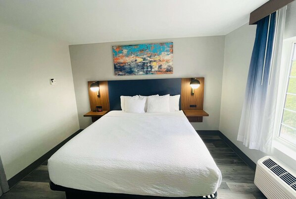 A hotel room with a large bed, two bedside tables with lamps, a painting on the wall, and a window with curtains. - La Quinta Inn & Suites by Wyndham Birmingham Homewood (Birmingham)