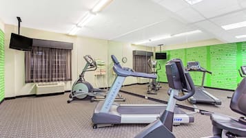 Une salle de sport équipée de tapis de course, de vélos d’appartement et d’un mur recouvert de miroirs.
