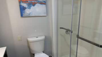 Une salle de bain avec une douche à parois de verre, des toilettes blanches et un tableau au mur.