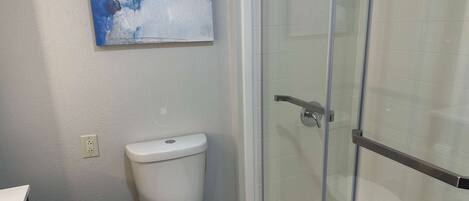 Un baño con cabina de ducha de vidrio, inodoro blanco y un cuadro en la pared.