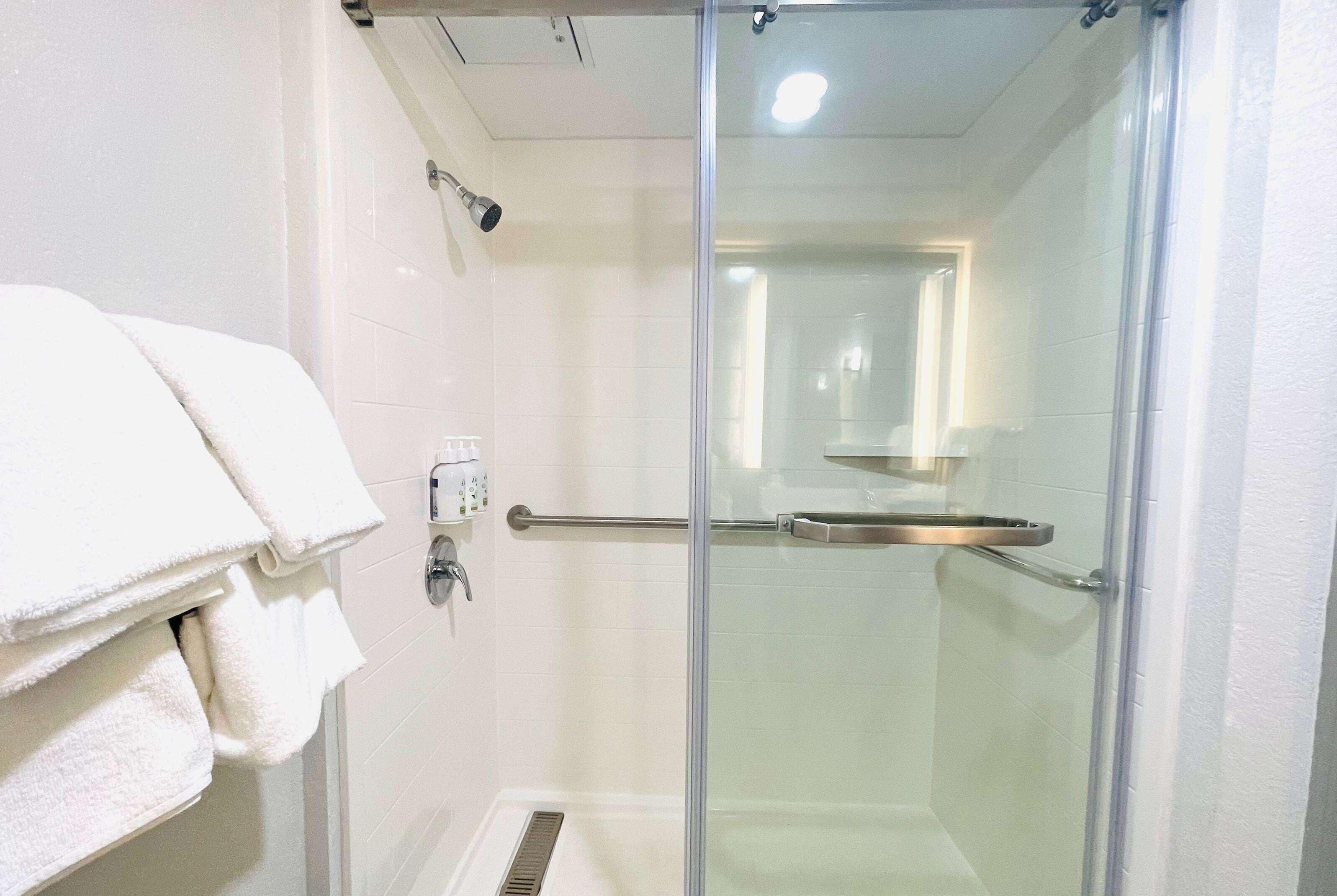 Un baño moderno con cabina de ducha de vidrio, un perchero con toallas dobladas y un secamanos visible.