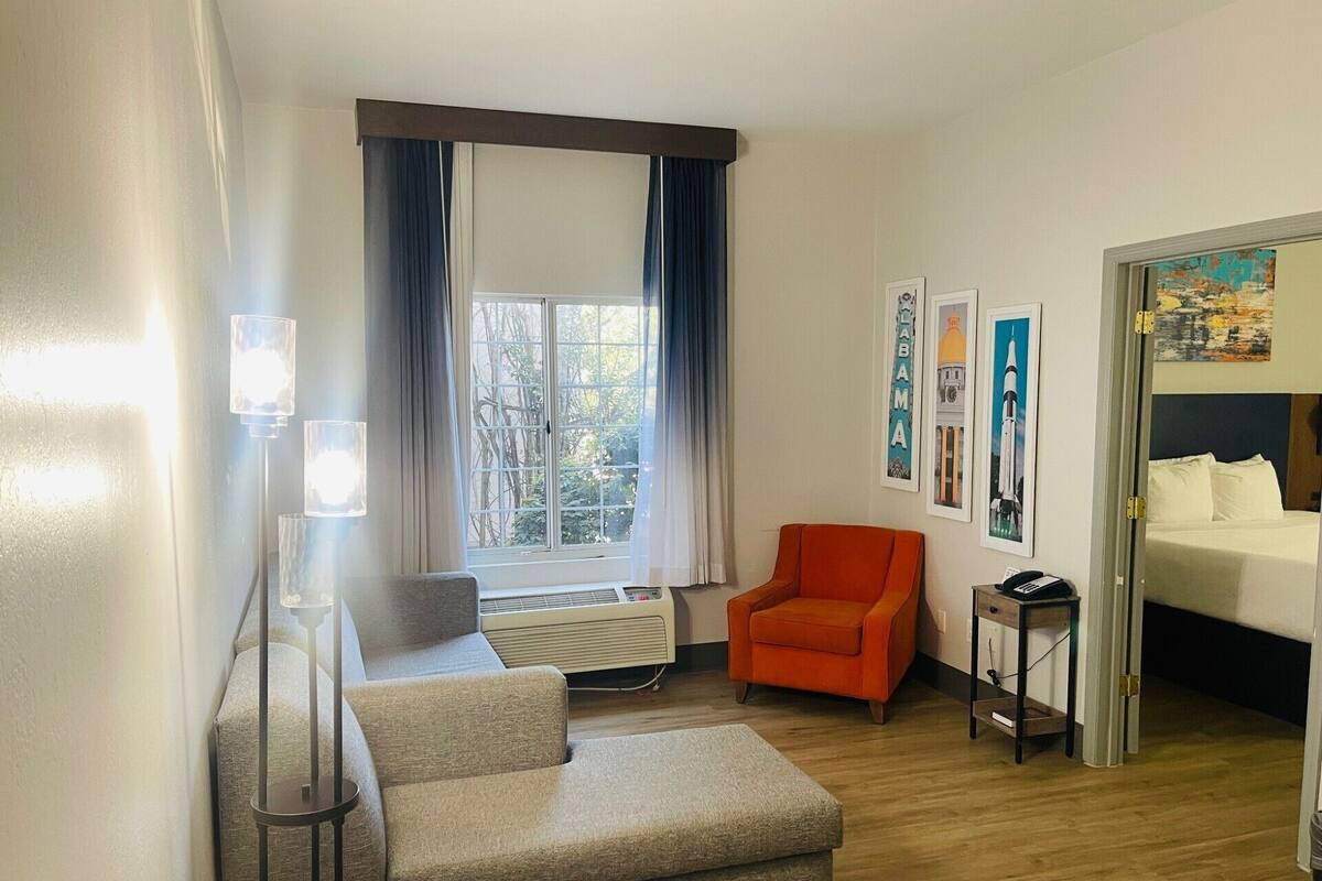 Een hotelkamer met een bank, fauteuil, bed en een raam met gordijnen.