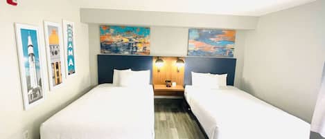 A hotel room with two single beds, a wooden headboard, a nightstand with two lamps, and artwork on the walls.