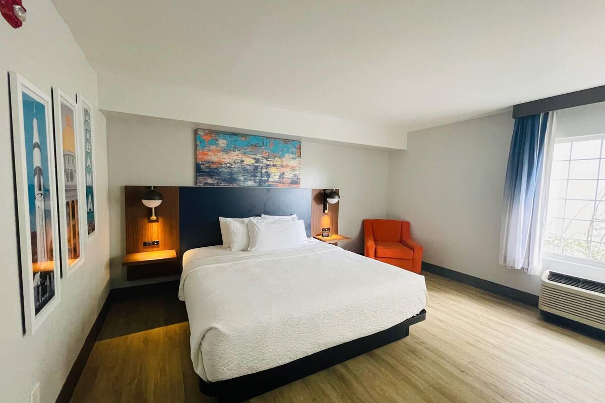 Een hotelkamer met een groot bed, een nachtkastje met een lamp, een stoel en een schilderij aan de muur.
