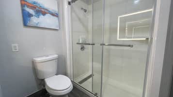 A modern bathroom with a toilet, a glass shower enclosure, and a painting on the wall.