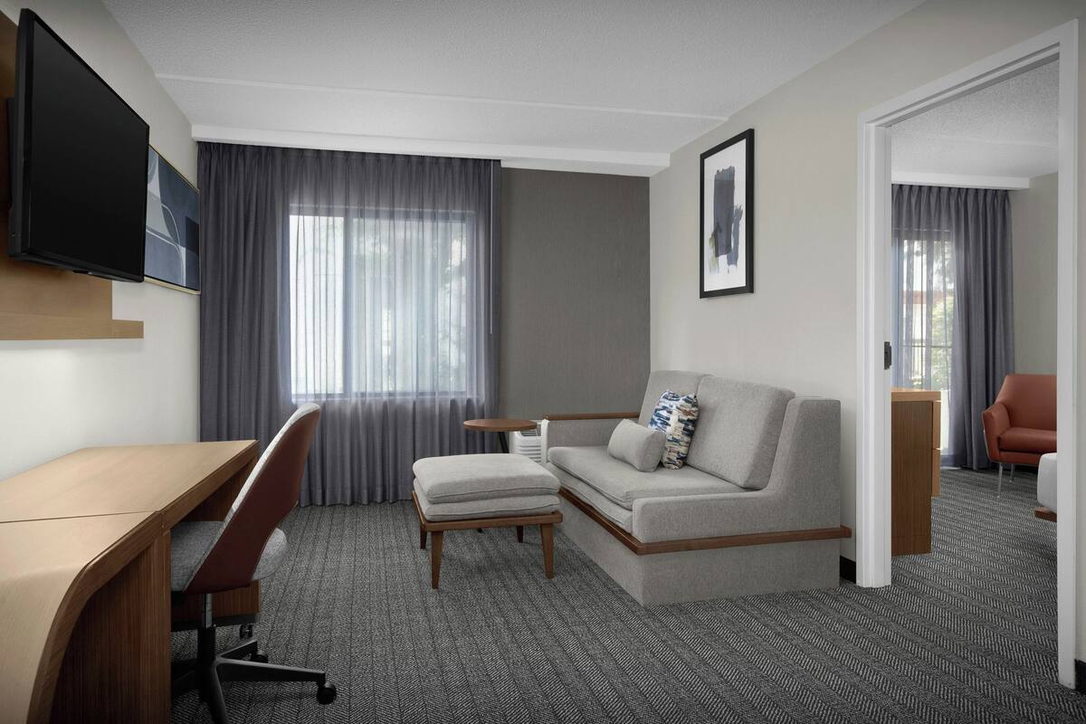 A hotel room with a desk, a sofa, a small table, and a TV mounted on the wall.