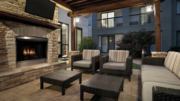 Un patio exterior con chimenea de piedra, mobiliario de mimbre y un televisor de pantalla plana montado sobre la chimenea.
