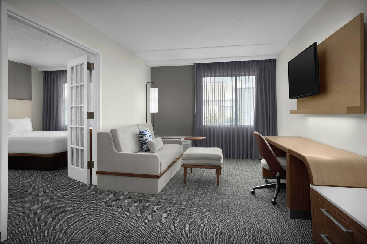 A hotel room with a bed, a sofa, a desk, a TV, and a window with curtains.