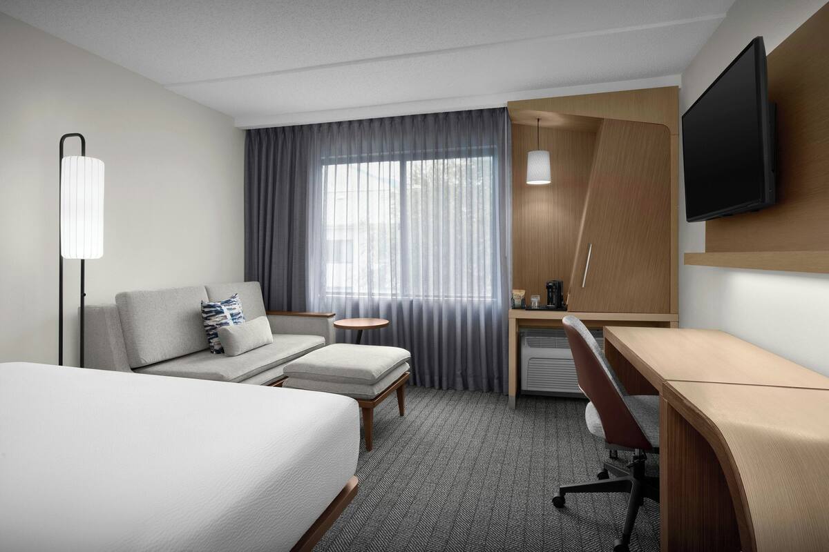 A hotel room with a bed, a desk, a chair, a TV, and a window with curtains.