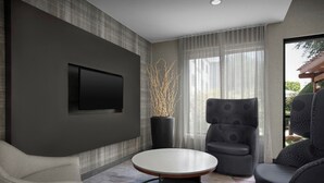 Una sala de estar moderna con una mesa redonda, dos sillones, un televisor de pantalla plana en la pared y un ventanal con cortinas translúcidas.