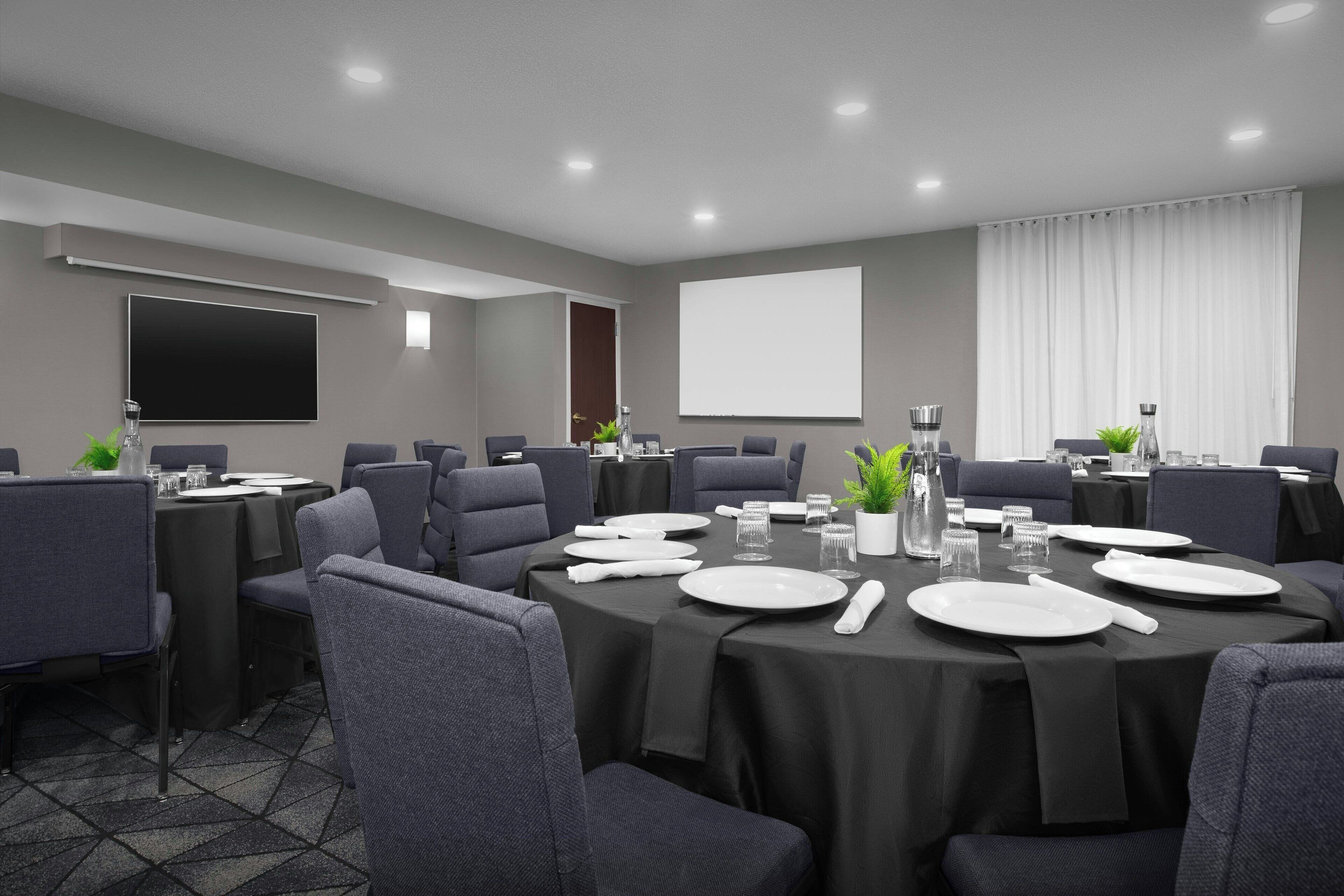 A conference room with round tables, gray chairs, and a large screen.