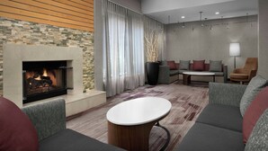 Un área de descanso moderna con chimenea, sofás, una mesa de centro y un amplio ventanal con cortinas.