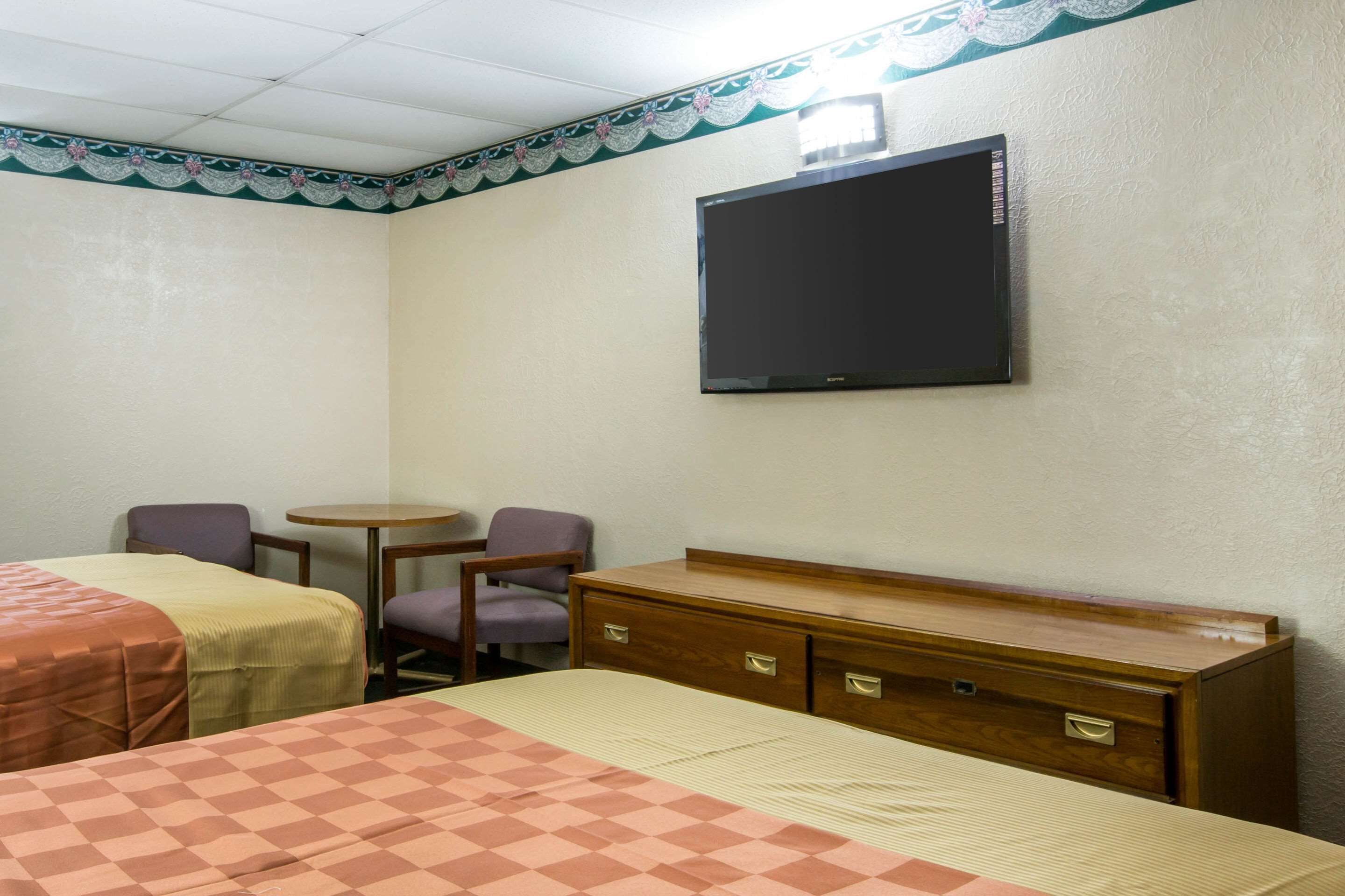 A hotel room with two beds, a desk, a chair, and a television on the wall.