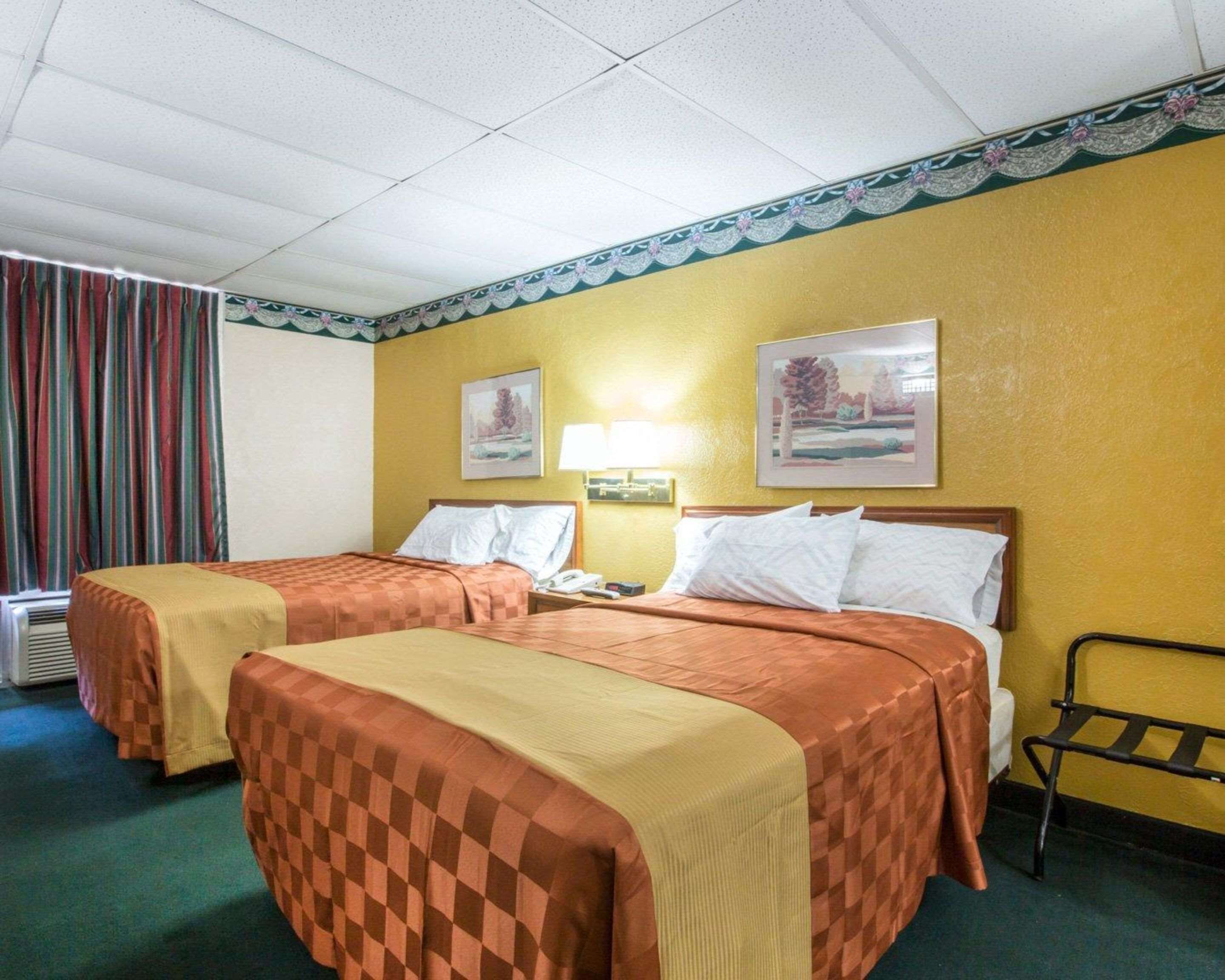 Habitación de hotel con dos camas, una mesita de noche con lámpara y una ventana con cortinas.
