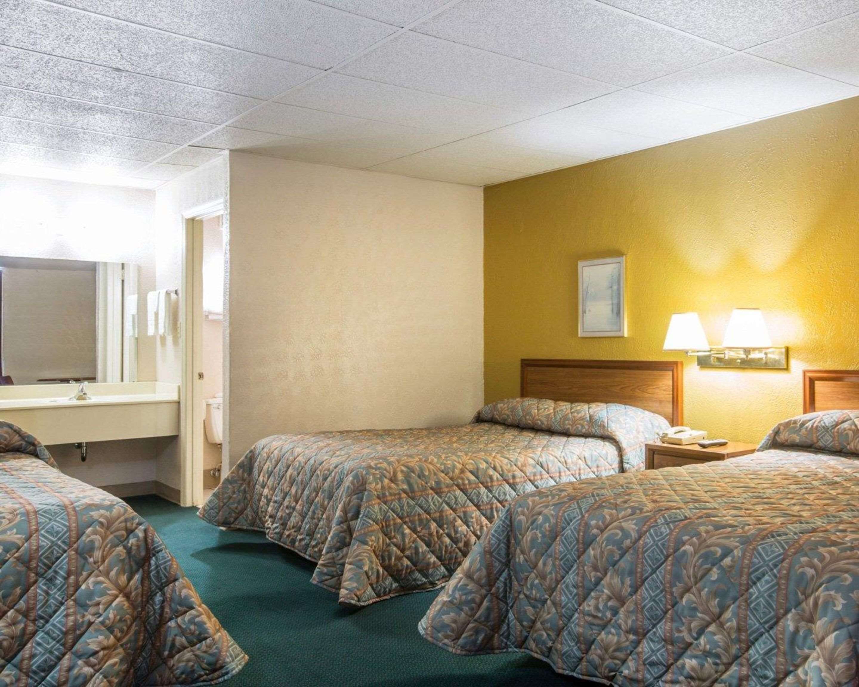 A hotel room with two beds, a bathroom with a mirror, and a nightstand with a lamp.
