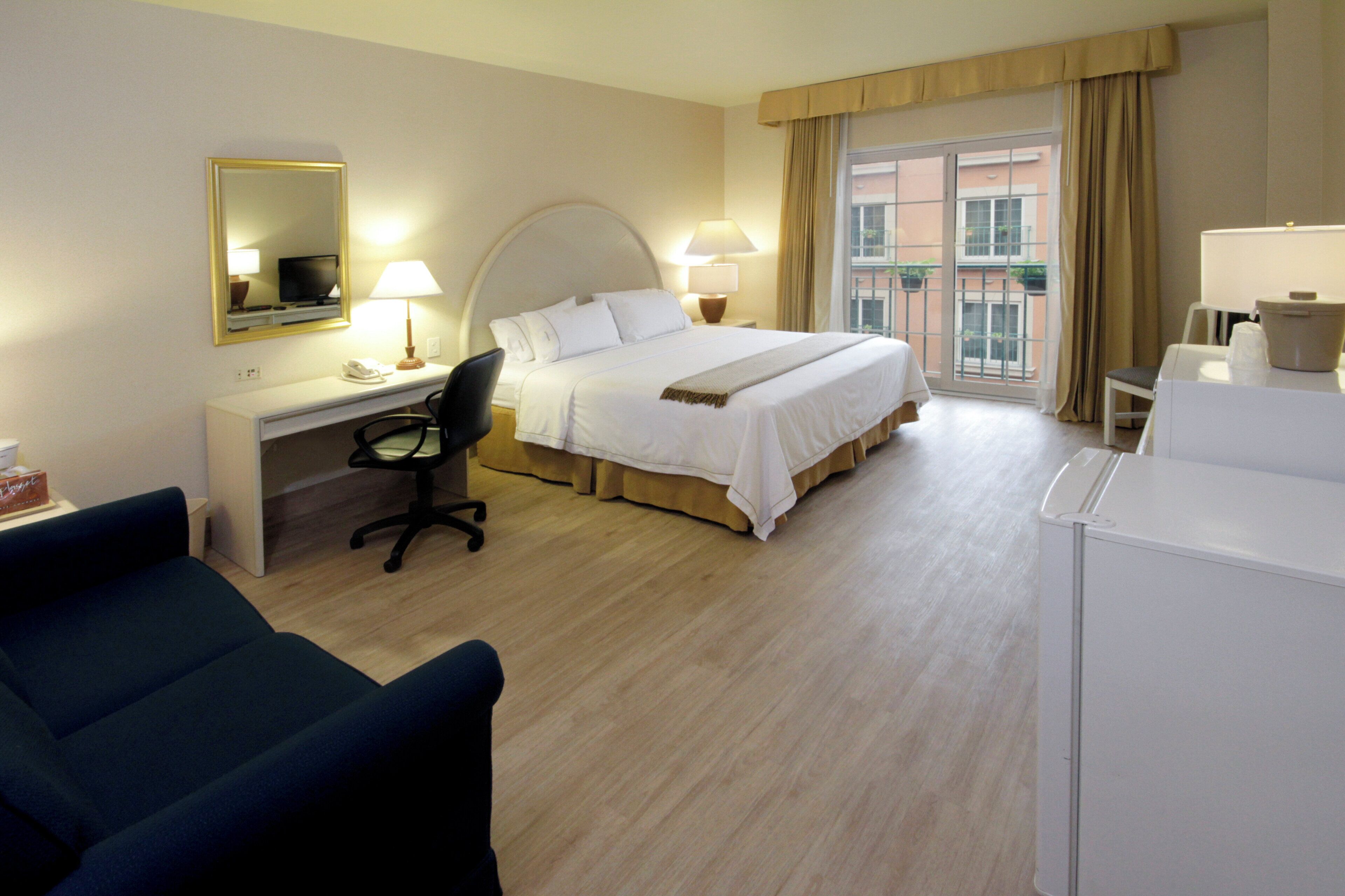 Una habitación de hotel con cama, escritorio, silla y un ventanal amplio.