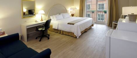 Una habitación de hotel con cama, escritorio, silla y un ventanal amplio.