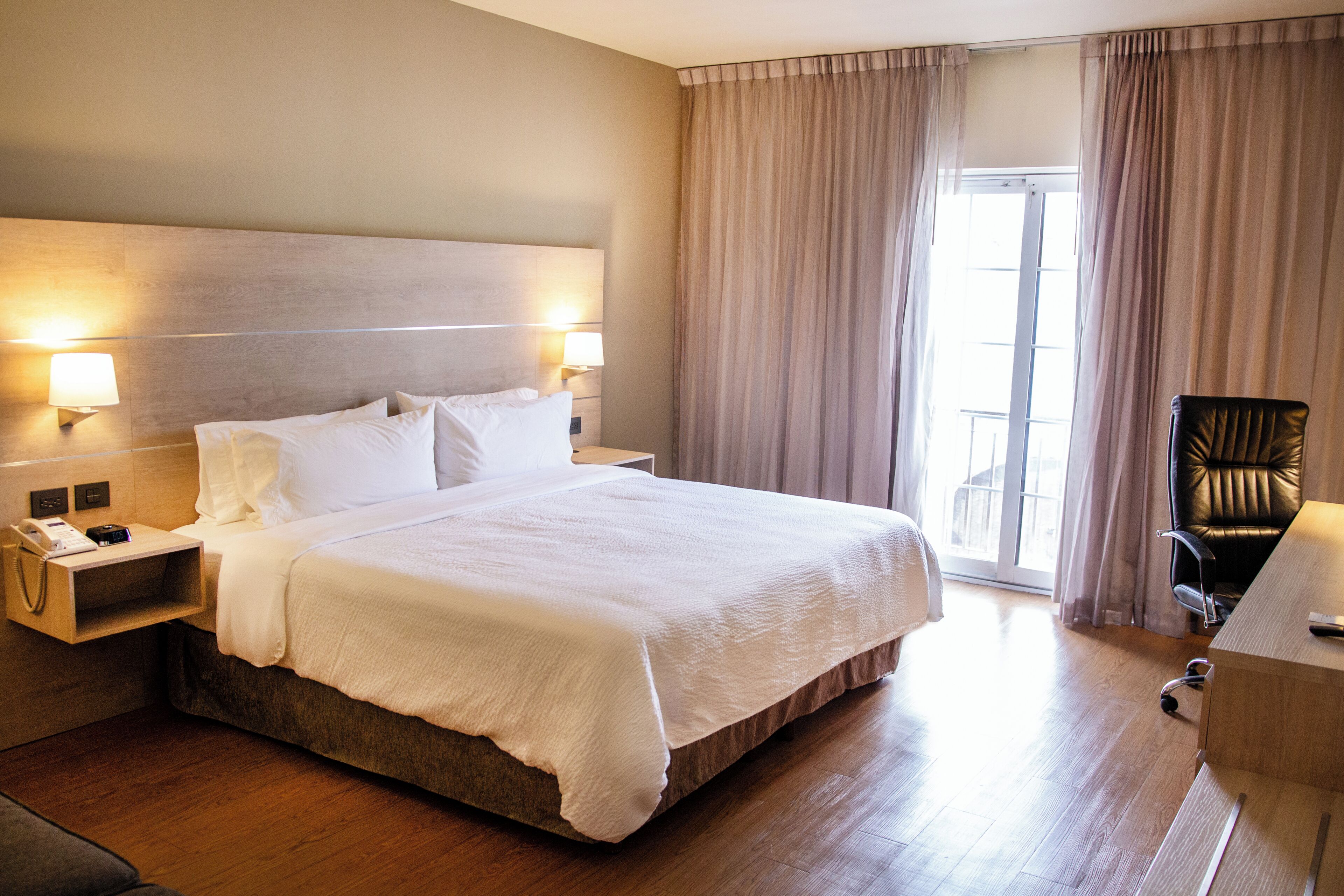 A hotel room with a bed, bedside table, lamp, and a chair.