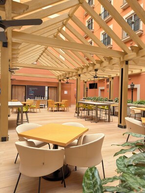 An indoor cafe with wooden tables and chairs, a wooden ceiling structure, and a view of a building with balconies. - Holiday Inn Express Torreon by IHG (Torreón)