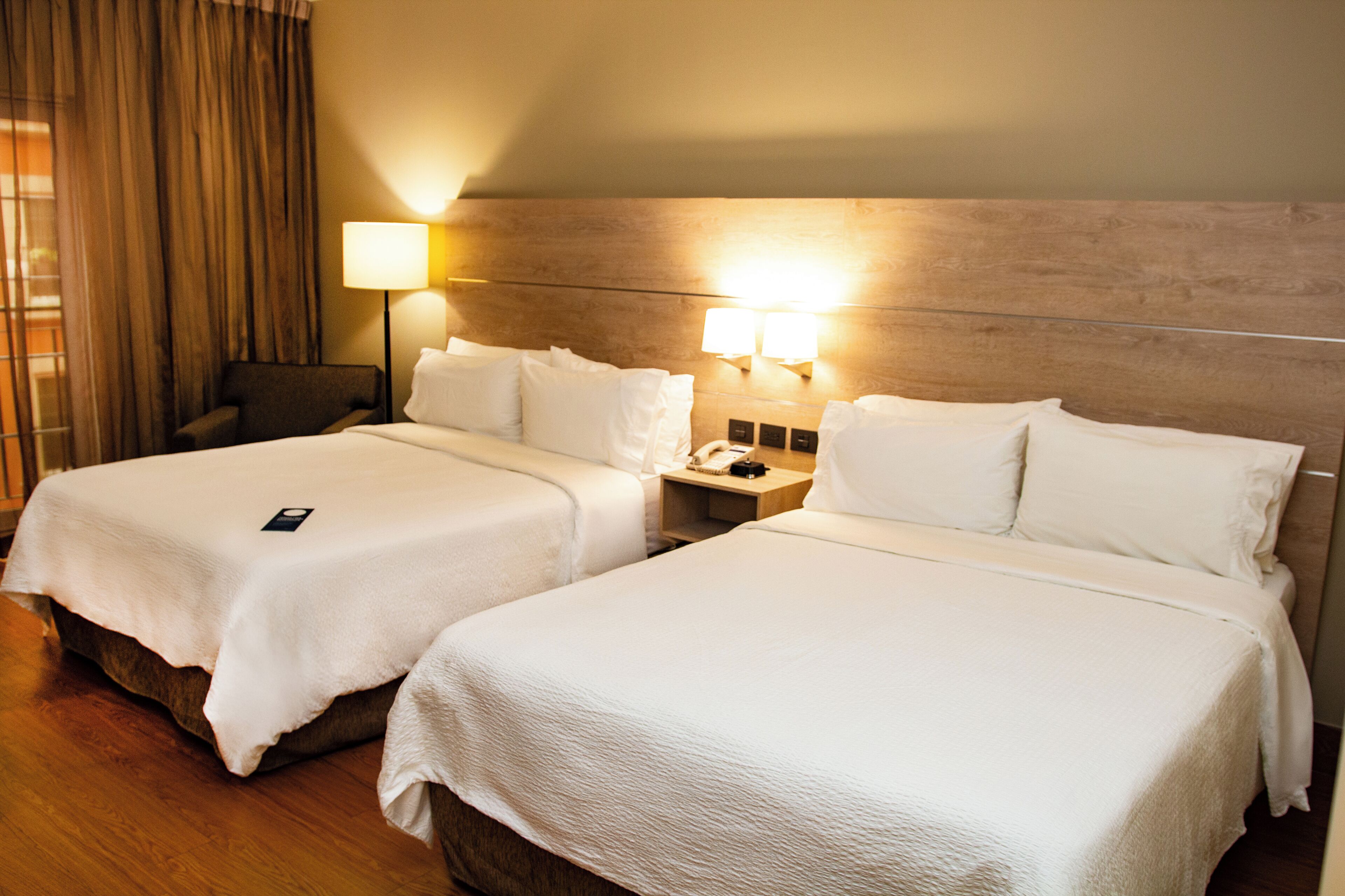 Habitación de hotel con dos camas, una mesita de noche con lámpara, teléfono y una silla.