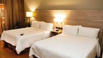 Habitación de hotel con dos camas, una mesita de noche con lámpara, teléfono y una silla.