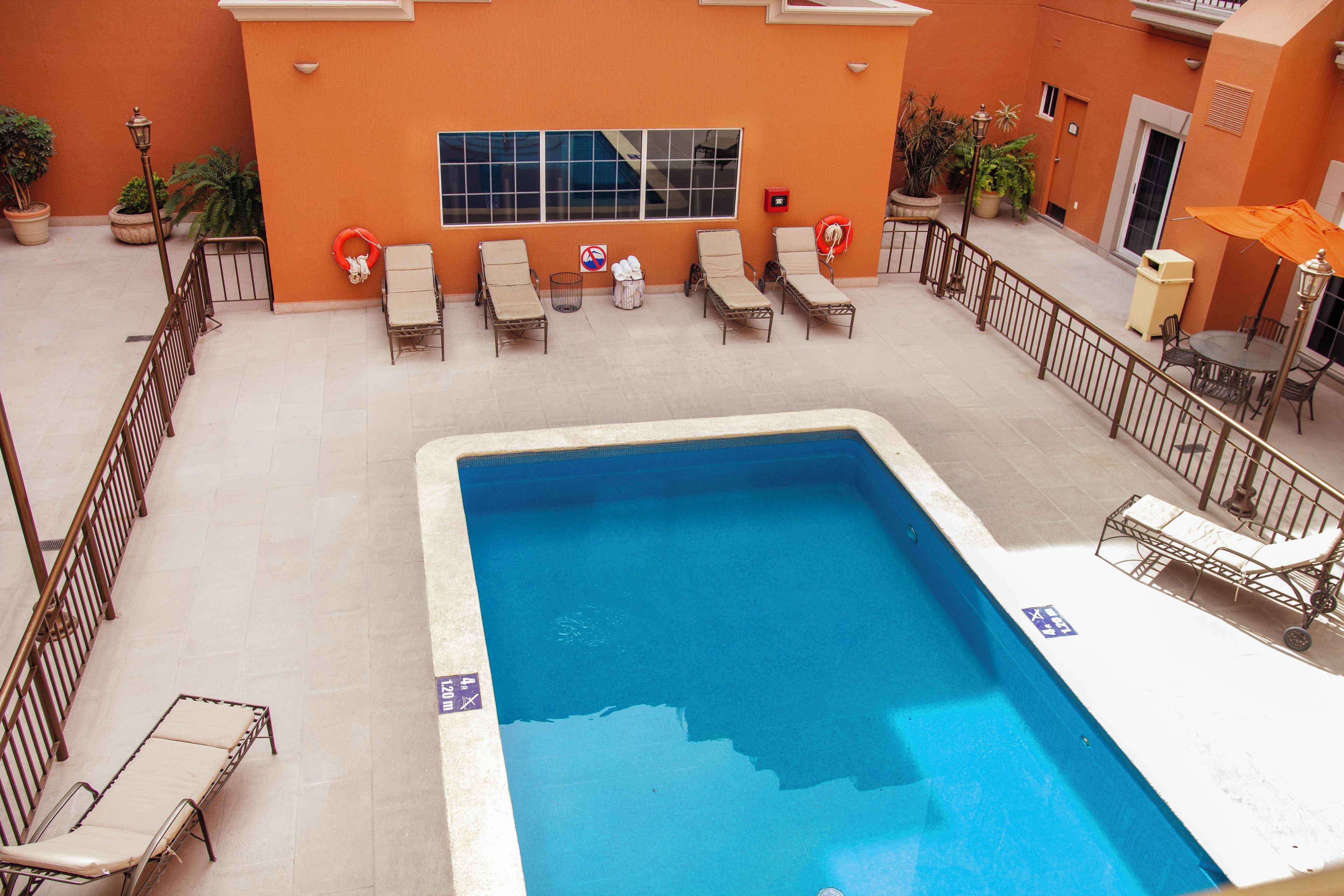 Una piscina con tumbonas y un flotador salvavidas, rodeada por una barandilla y plantas en macetas.
