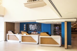A hotel reception area with a modern design, featuring a reception desk, a blue accent wall, and a visible refrigerator in the background.