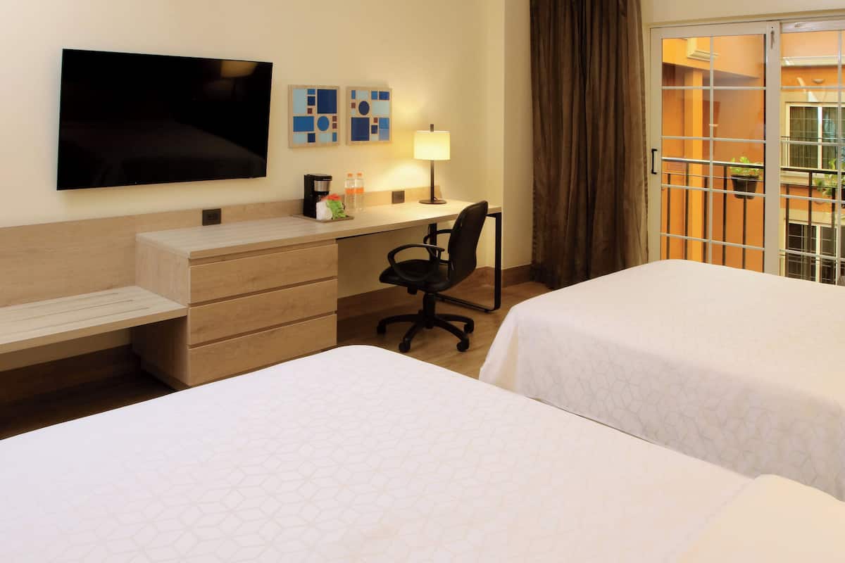 A hotel room with two beds, a desk with a chair, a TV, and a window with curtains.