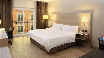 A hotel room with a large bed, a desk, a chair, and a view of the outside balcony.