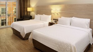 Habitación de hotel con dos camas, un sofá, una mesita de noche con teléfono y ventana con vistas al exterior.