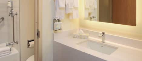 A modern bathroom with a white sink, a mirror, and a shower area.
