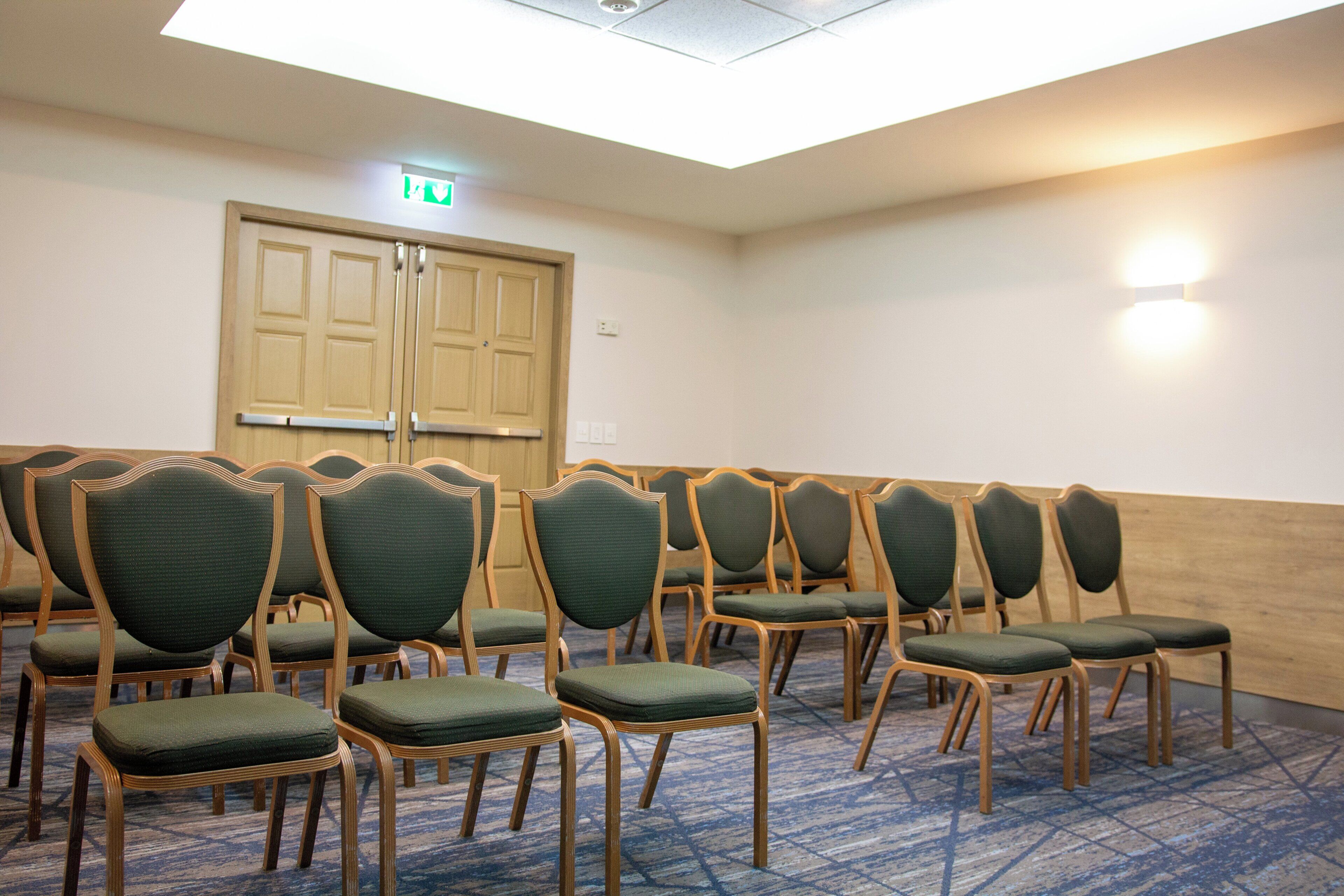 Un salón de conferencias con filas de sillas, una puerta de madera y un accesorio de iluminación en la pared.