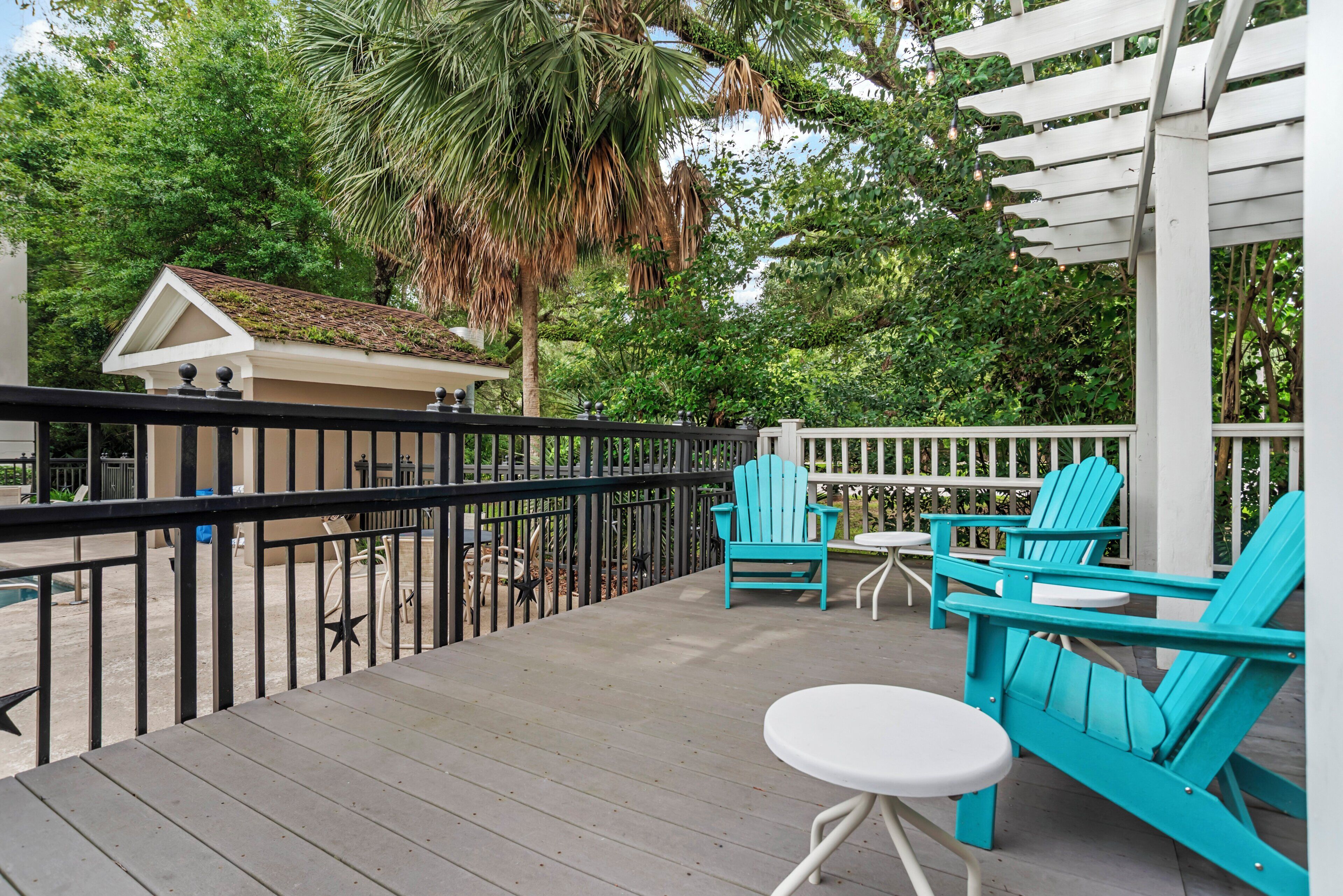 A wooden deck with a white railing, turquoise Adirondack chairs, and a small table.