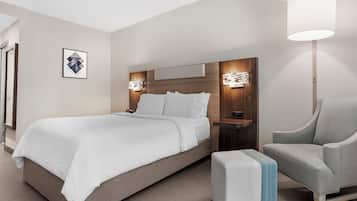 A modern hotel room with a bed, bedside tables, a chair, and a lamp.