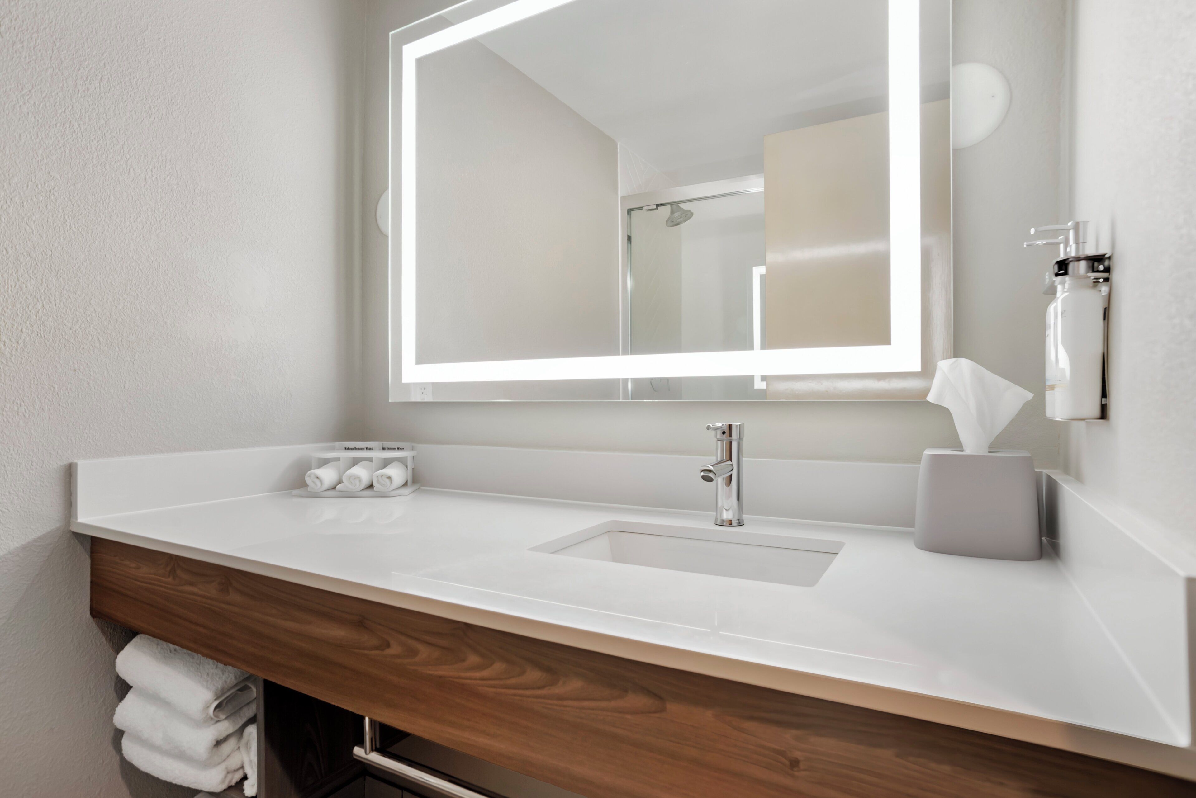 A bathroom with a white sink, a mirror, and a towel dispenser.