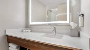 A bathroom with a white sink, a mirror, and a towel dispenser.