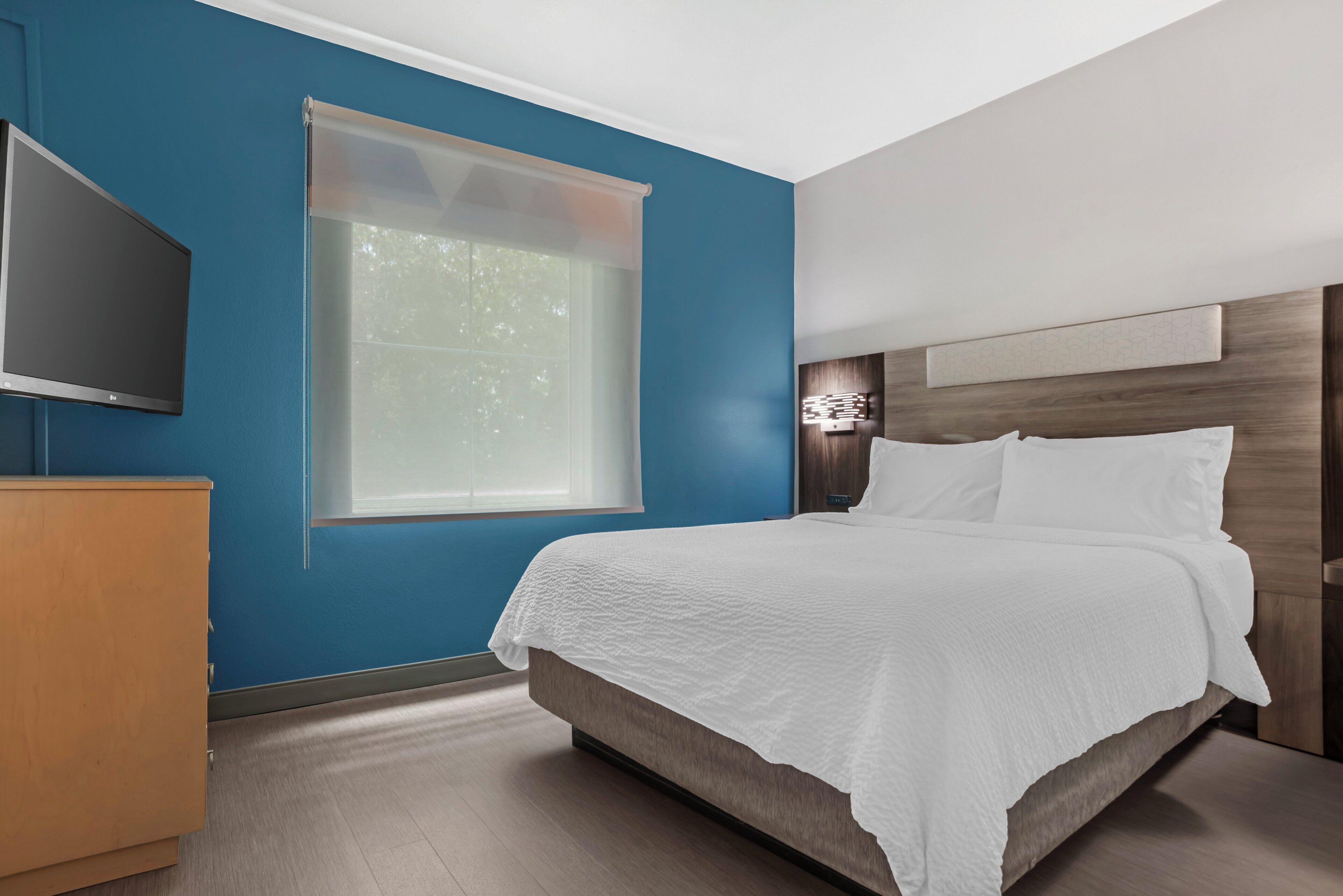 Une chambre à coucher avec un lit, un téléviseur, une fenêtre et un luminaire fixé au mur.