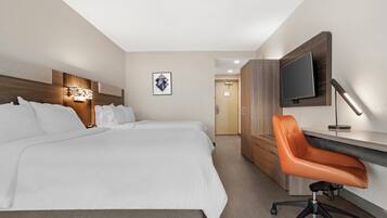 A hotel room with a large bed, a desk with a chair, a TV mounted on the wall, and a framed picture on the wall.
