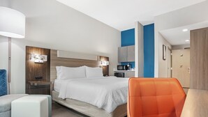 A modern hotel room with a bed, nightstands, a desk, a chair, and a wardrobe.