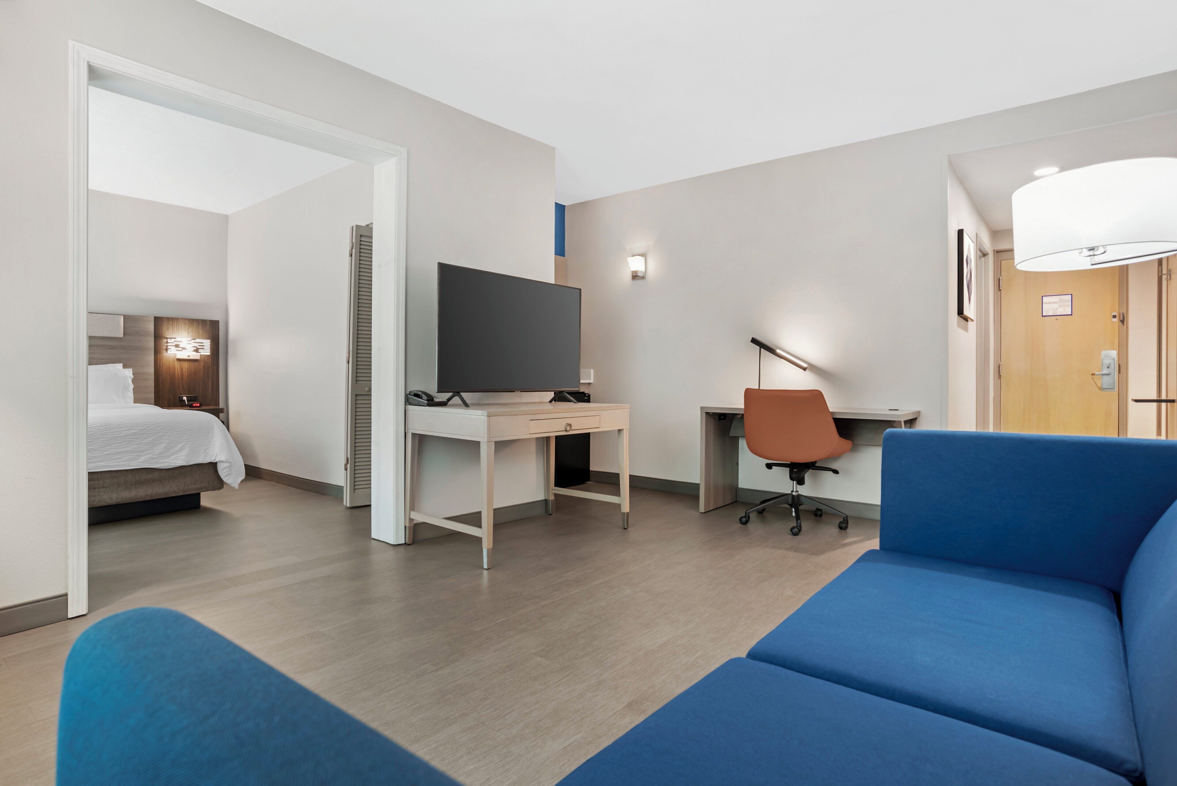 Une chambre d’hôtel avec un lit, un bureau avec une télévision, un canapé bleu et une porte.