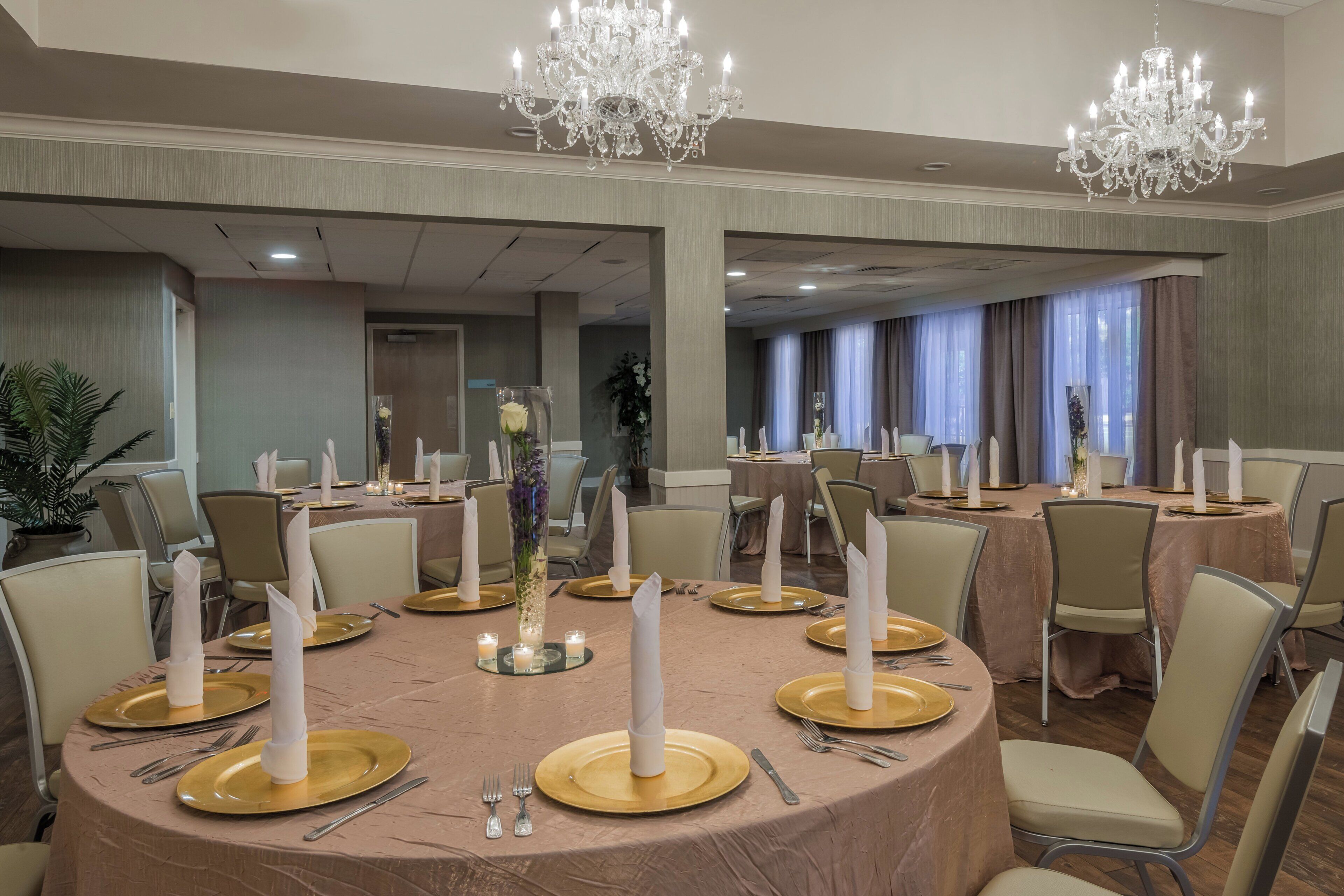 A banquet hall with round tables, gold chargers, white napkins, and crystal chandeliers.