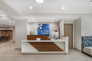 A hotel reception desk with a blue wall art, a wooden counter, and a sign indicating 'Holiday Inn Express.'