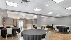 A conference room with round tables, white chairs, chandeliers, and an American flag.