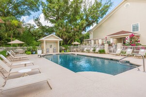 A swimming pool with lounge chairs and umbrellas, surrounded by trees and a building.