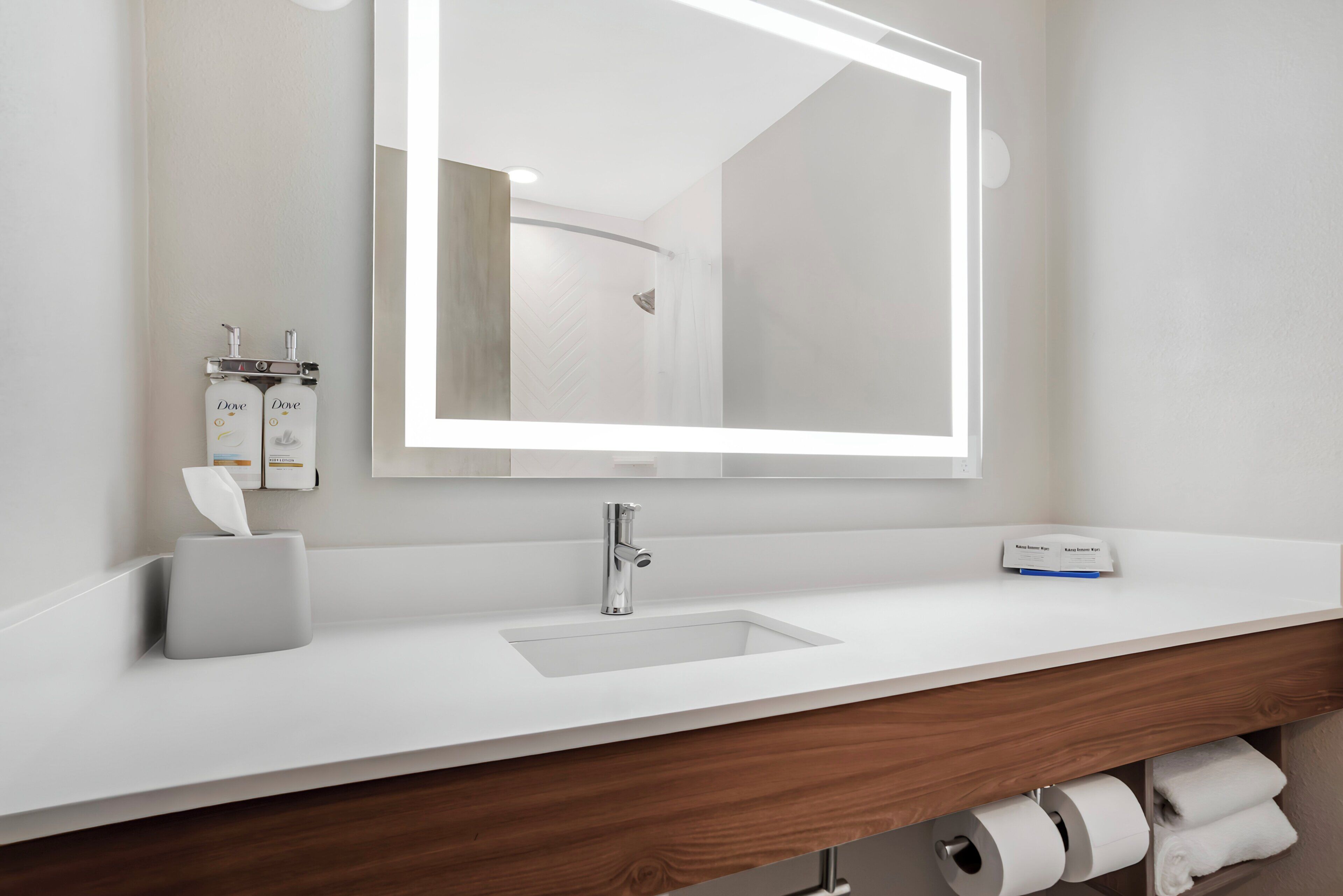 Ein modernes Badezimmer mit einem weißen Waschbecken, einem Spiegel und einer Holzwaschkommode.