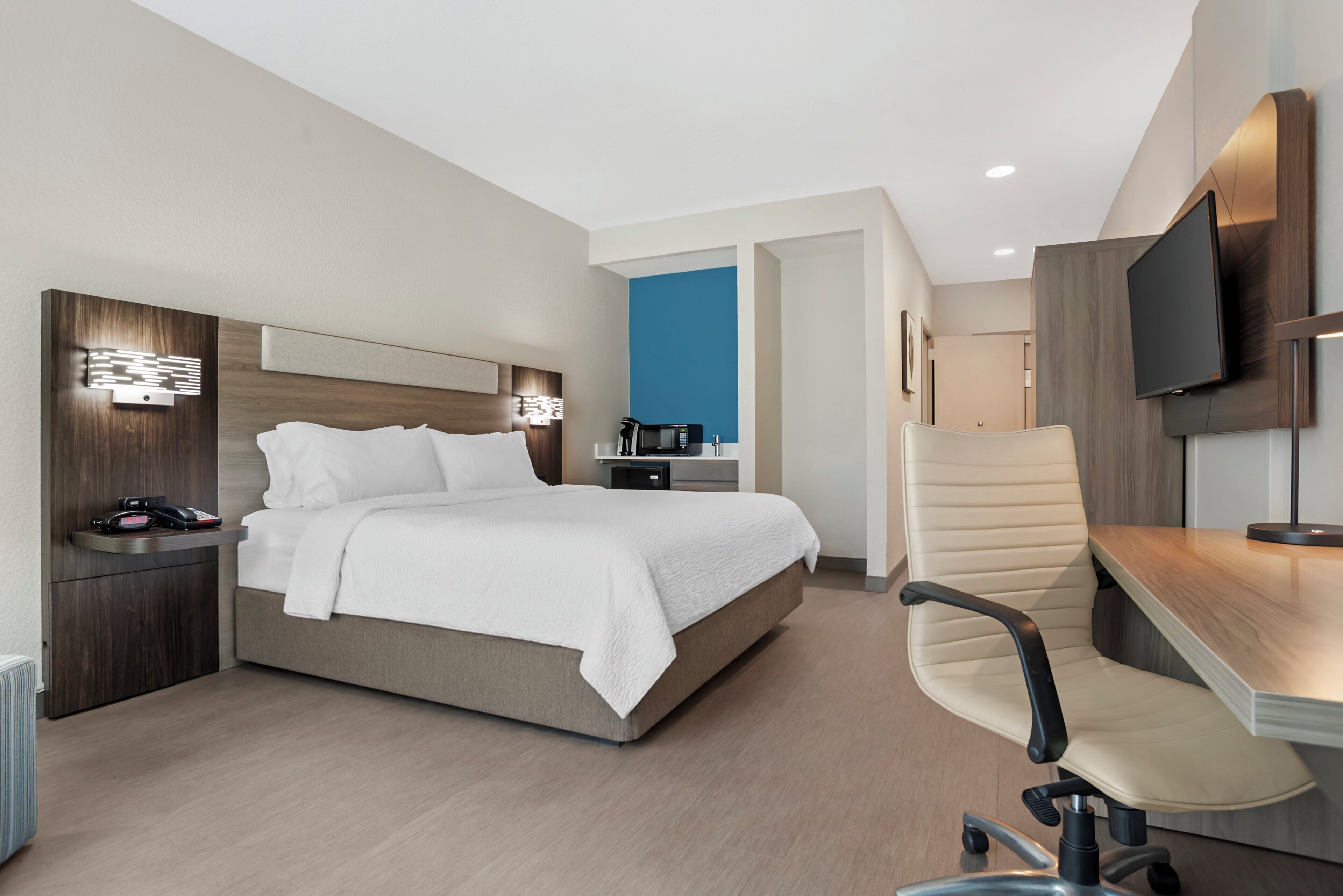Una habitación de hotel moderna con cama, escritorio, silla y televisor.