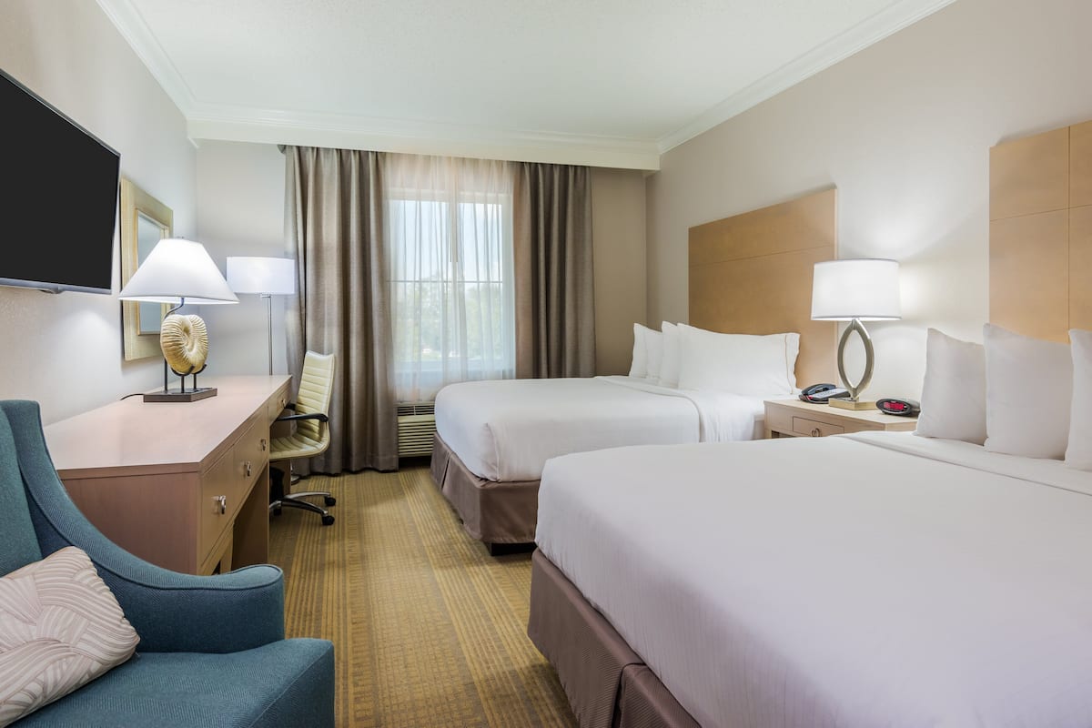 A hotel room with two beds, a desk with a chair, a TV, and a lamp.