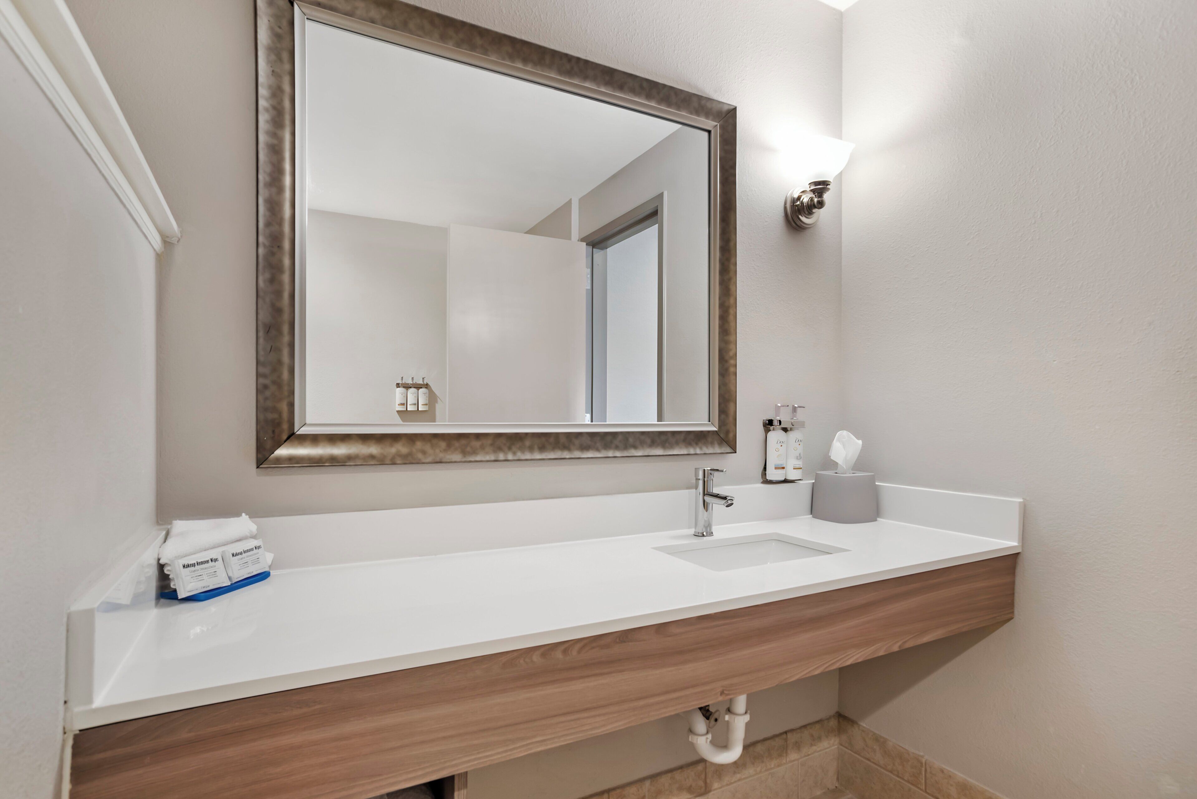 Une salle de bain avec un lavabo blanc, un meuble-lavabo en bois, un miroir avec un cadre en bois, un distributeur de serviettes et un distributeur de savon.