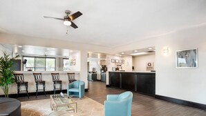 A modern hotel lobby with a seating area, a bar, and a kitchen in the background.